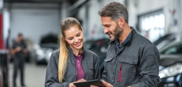 Zwei Mechaniker im Gespräch mit Blick auf ein Tablet.