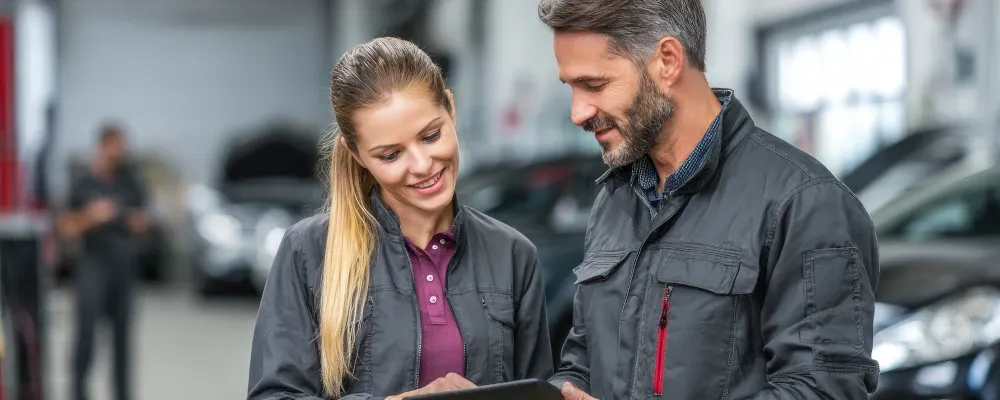 Zwei Mechaniker im Gespräch mit Blick auf ein Tablet.
